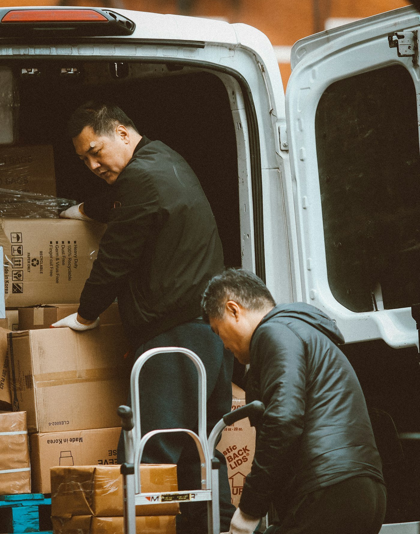 Two team members unloading boxes from a delivery van with a hand truck